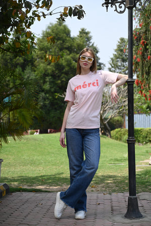 Woman wearing a light pink slogan t-shirt with “Merci” print – round neck casual top for women